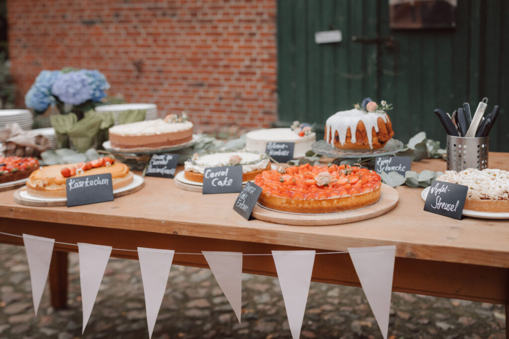 Liebevoll angerichtetes Kuchenbuffet von Saltkrokran Oldenburg waehrend des Sektempfangs auf dem Hof Schweers. Authentische Hochzeitsfotografie und stilvolle Hochzeitsdetails vom Hochzeitsfotograf Oldenburg.