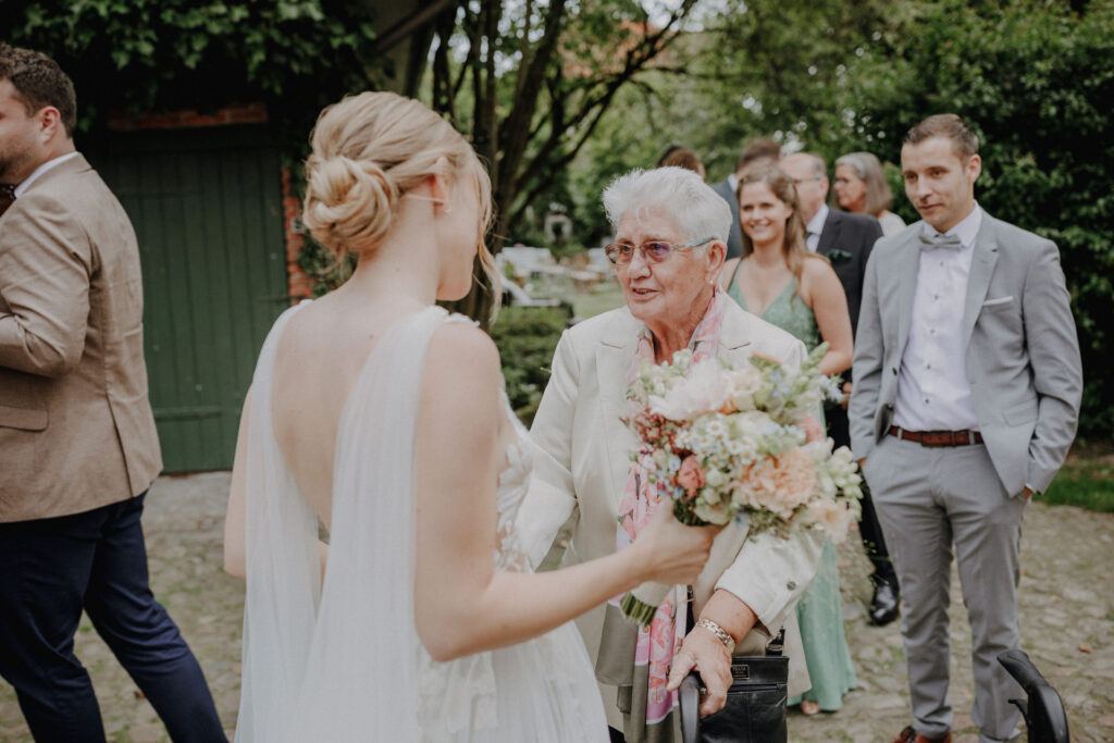 Braut nimmt die Glueckwuensche einer Hochzeitsgaestin nach der freien Trauung auf dem Hof Schweers entgegen. Authentische Hochzeitsfotografie voller Emotionen vom Hochzeitsfotograf Oldenburg.