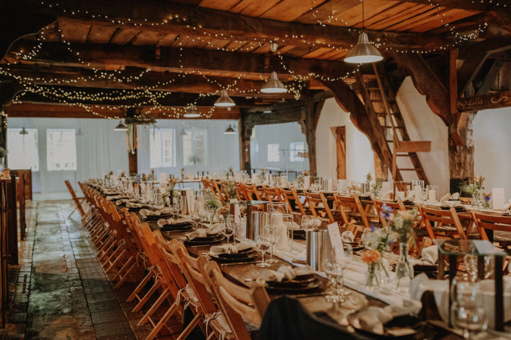 Stilvoll dekorierte Hochzeitsscheune auf dem Hof Schweers mit festlich gedeckten Tischen und stimmungsvoller Lichterkette. Authentische Hochzeitsfotografie und elegante Hochzeitsfotos vom Hochzeitsfotograf Oldenburg.