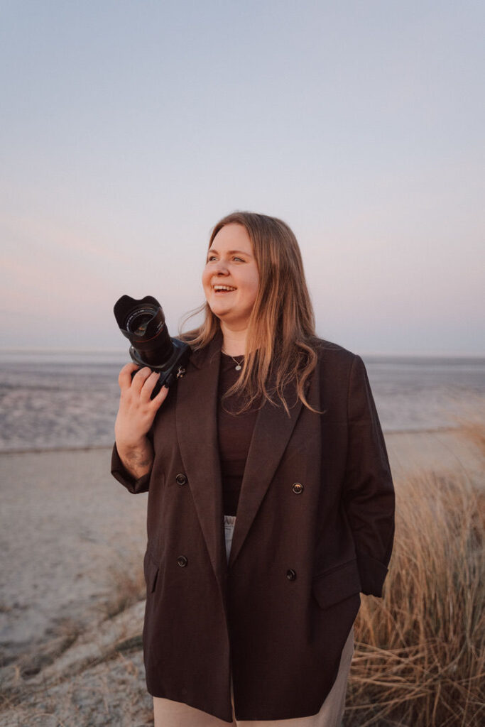 Anna-Lena Berreth, Hochzeitsfotograf aus Oldenburg, mit Kamera am Strand bei Sonnenuntergang – spezialisiert auf natürliche und emotionale Hochzeitsfotografie.