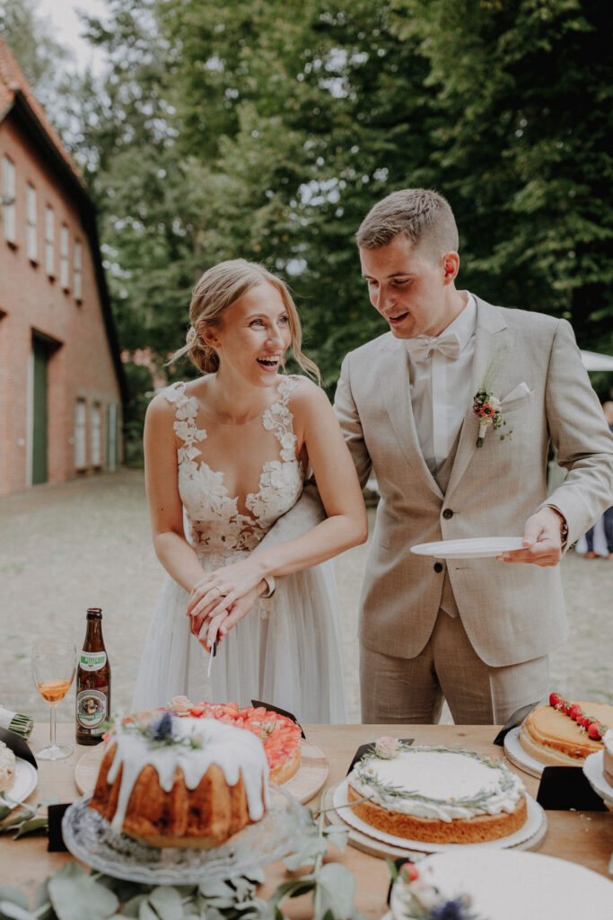 Braut und Braeutigam schneiden gemeinsam die Hochzeitstorte waehrend ihrer Feier im Hof Schweers. Authentisches Hochzeitsshooting und emotionale Hochzeitsfotografie in Oldenburg.