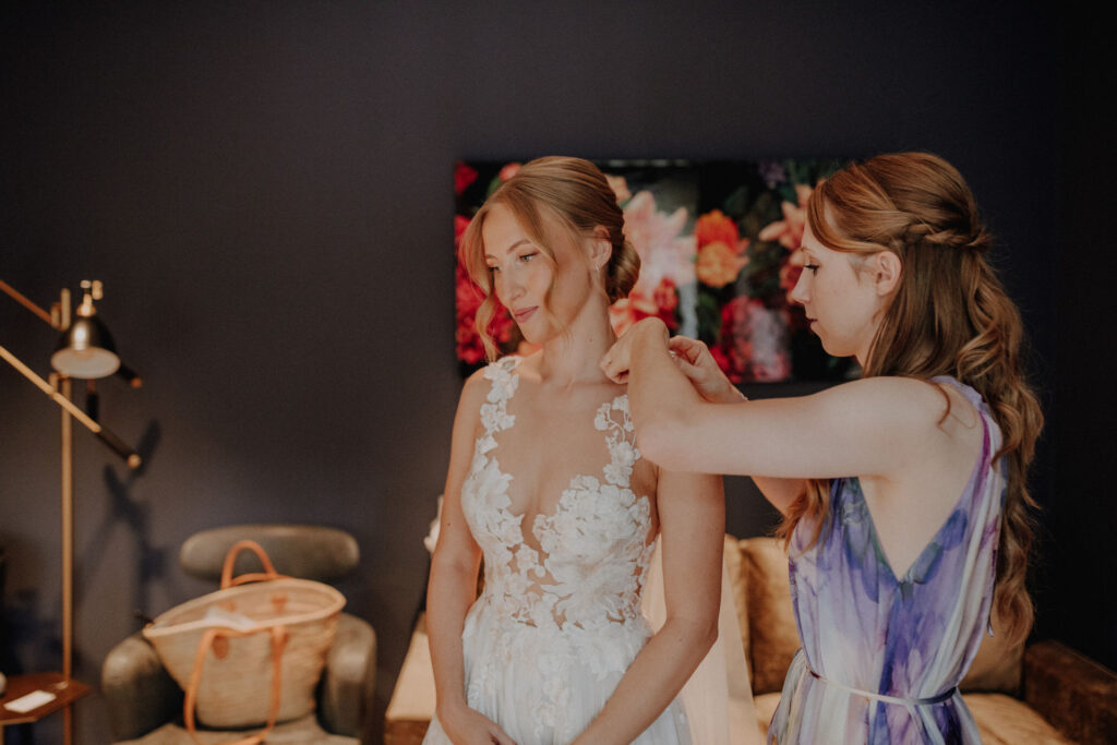 Braut wird waehrend des Getting Readys beim Anlegen ihres Brautkleides begleitet. Authentische Hochzeitsfotos einer freien Trauung in Oldenburg mit natuerlicher Hochzeitsfotografie.