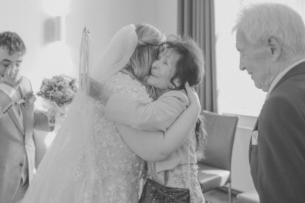 Die Braut umarmt nach der Trauung ein Familienmitglied voller Emotionen, während weitere Angehörige den Moment miterleben. Authentische Hochzeitsfotografie und emotionale Hochzeitsfotos vom Hochzeitsfotograf Oldenburg.